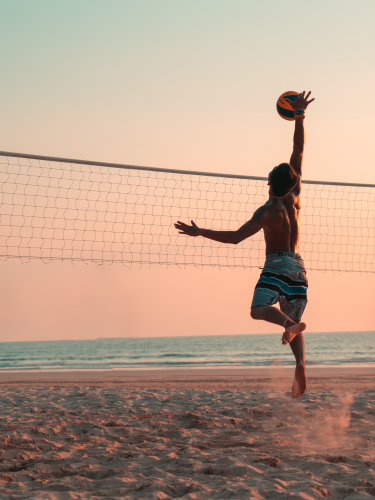 Sport de balle et vue : homme jouant au beach volleyball sur la plage au coucher de soleil