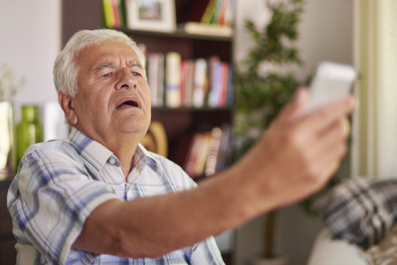 A man struggles to see his phone due to presbyopia so stretches his arm out to see more clearly