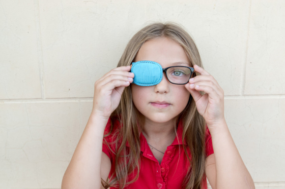 Little girl wearing glasses with an eye patch to correct strabismus