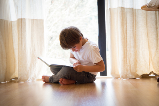 Little boy sat on floor struggling to read book due to astigmatism