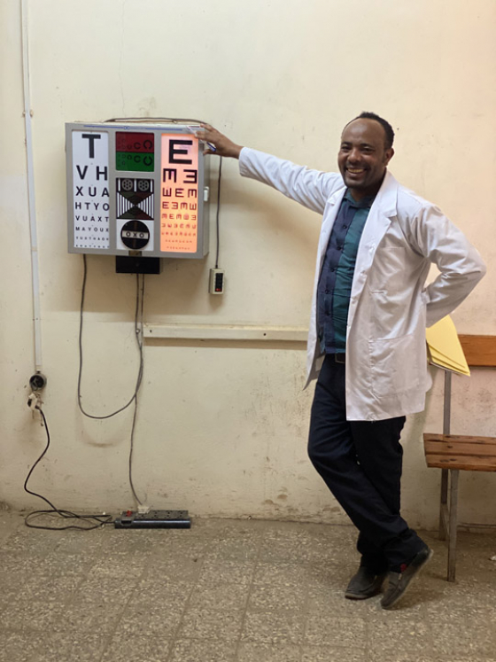 An optician in Ethiopia stood next to eye examination chart